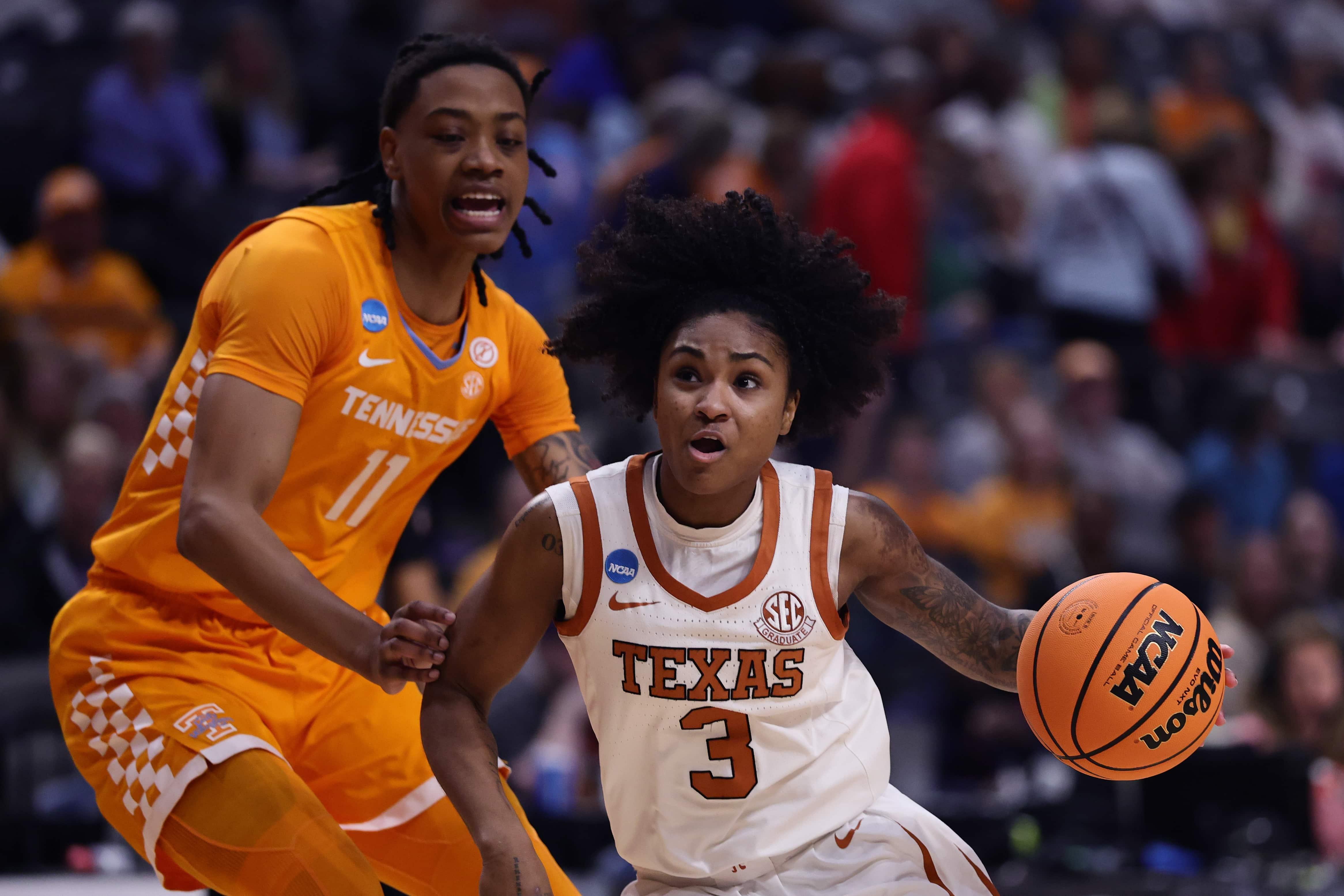 A women's basketball player dribbles around a defender.